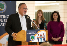 Man speaking at a podium with two females behind him